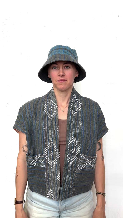 Person wearing a white diamond and blue and gray stripped short sleeve jacket and matching hat, turning around to show all sides. 