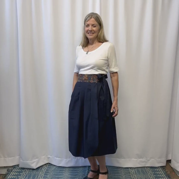 Woman slowly spins modeling a dusk midi skirt styled with a white tee in front of a white background. 